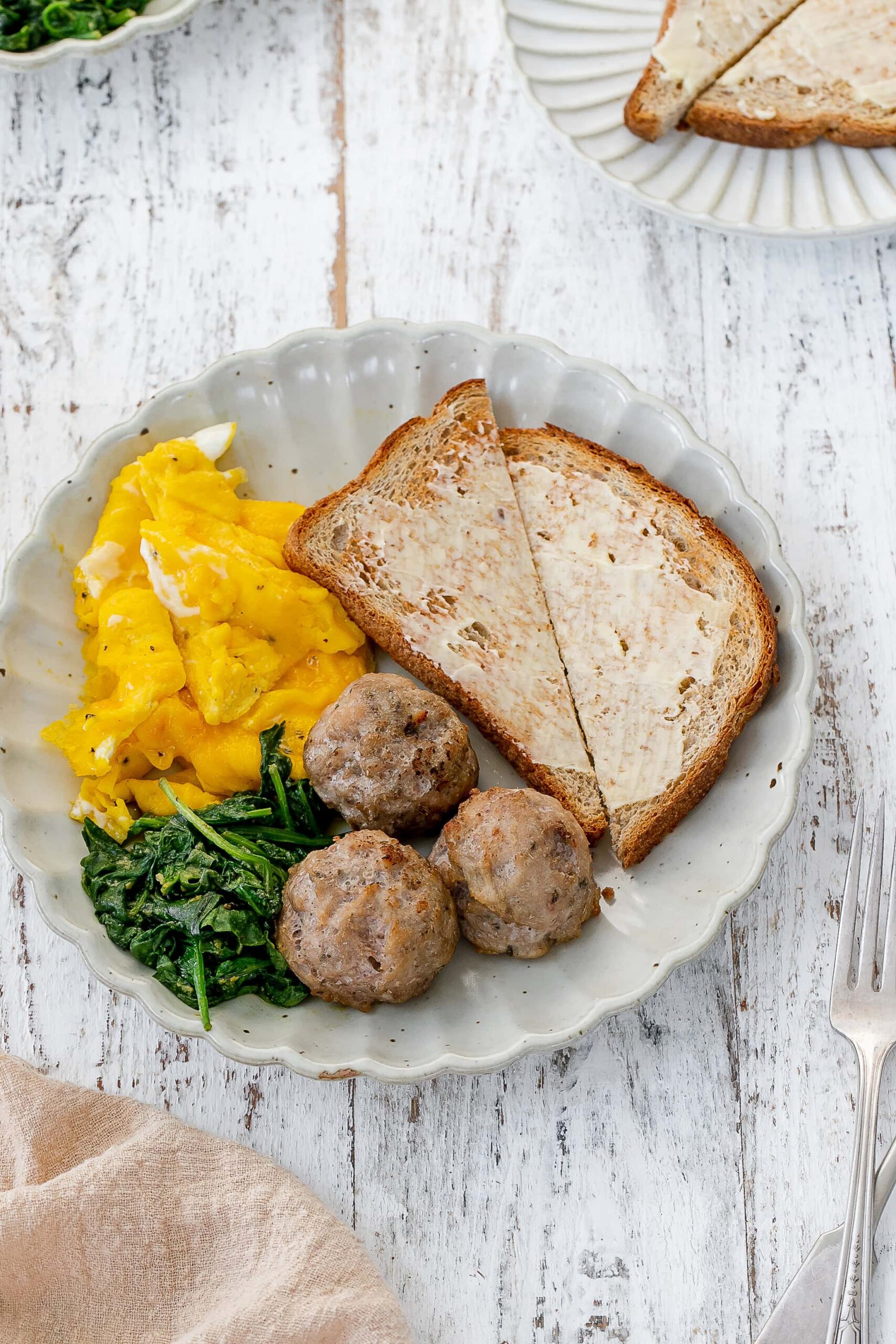 breakfast meatballs on a plate with eggs, spinach and toast.