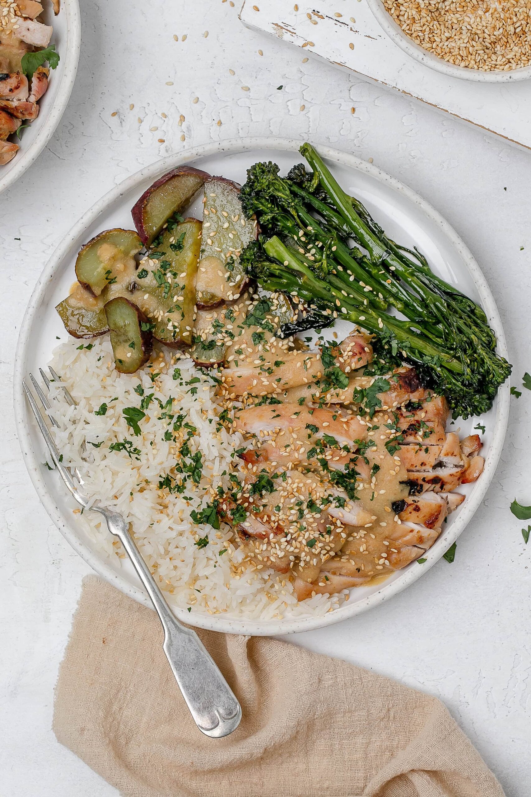 miso butter chicken thighs on a plate with rice and veggies.