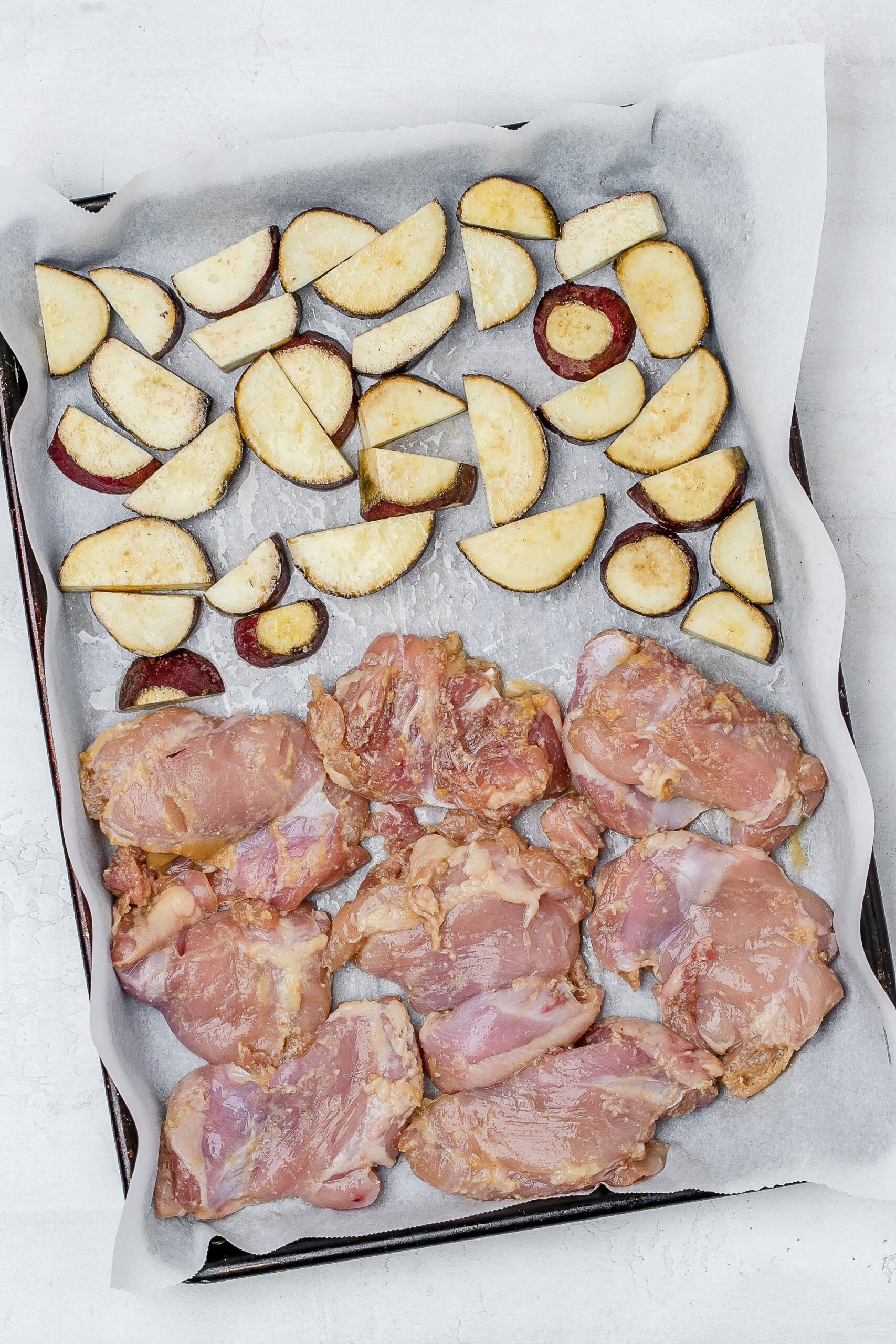 miso chicken thighs on baking sheet with sweet potato.