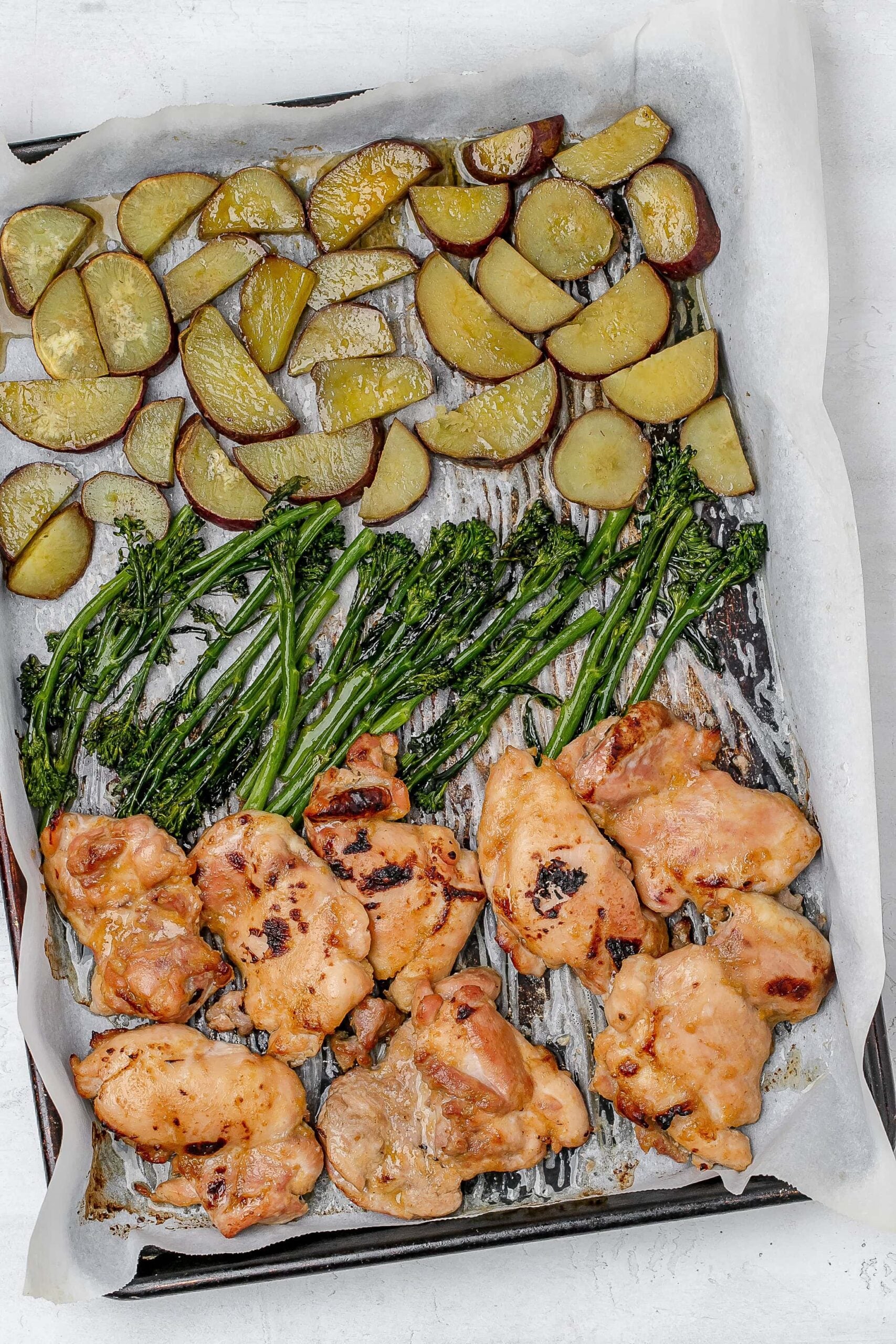 miso butter chicken thighs on baking sheet with sweet potato and broccolini. 