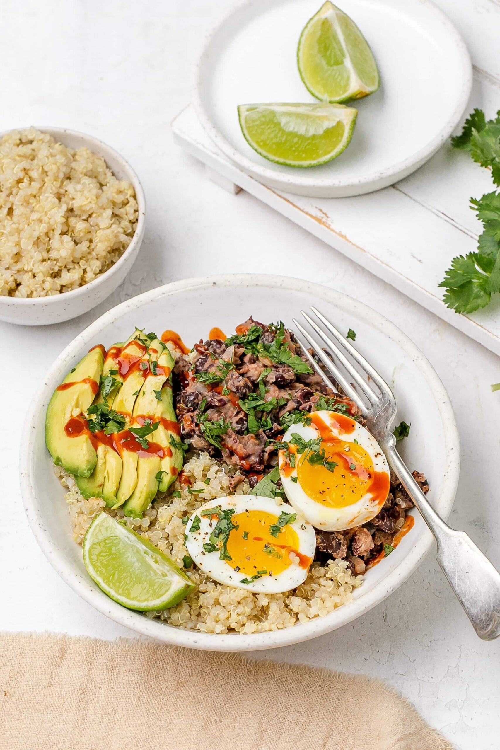 black bean, quinoa and egg breakfast bowl with avocado and hot sauce drizzled on top. 