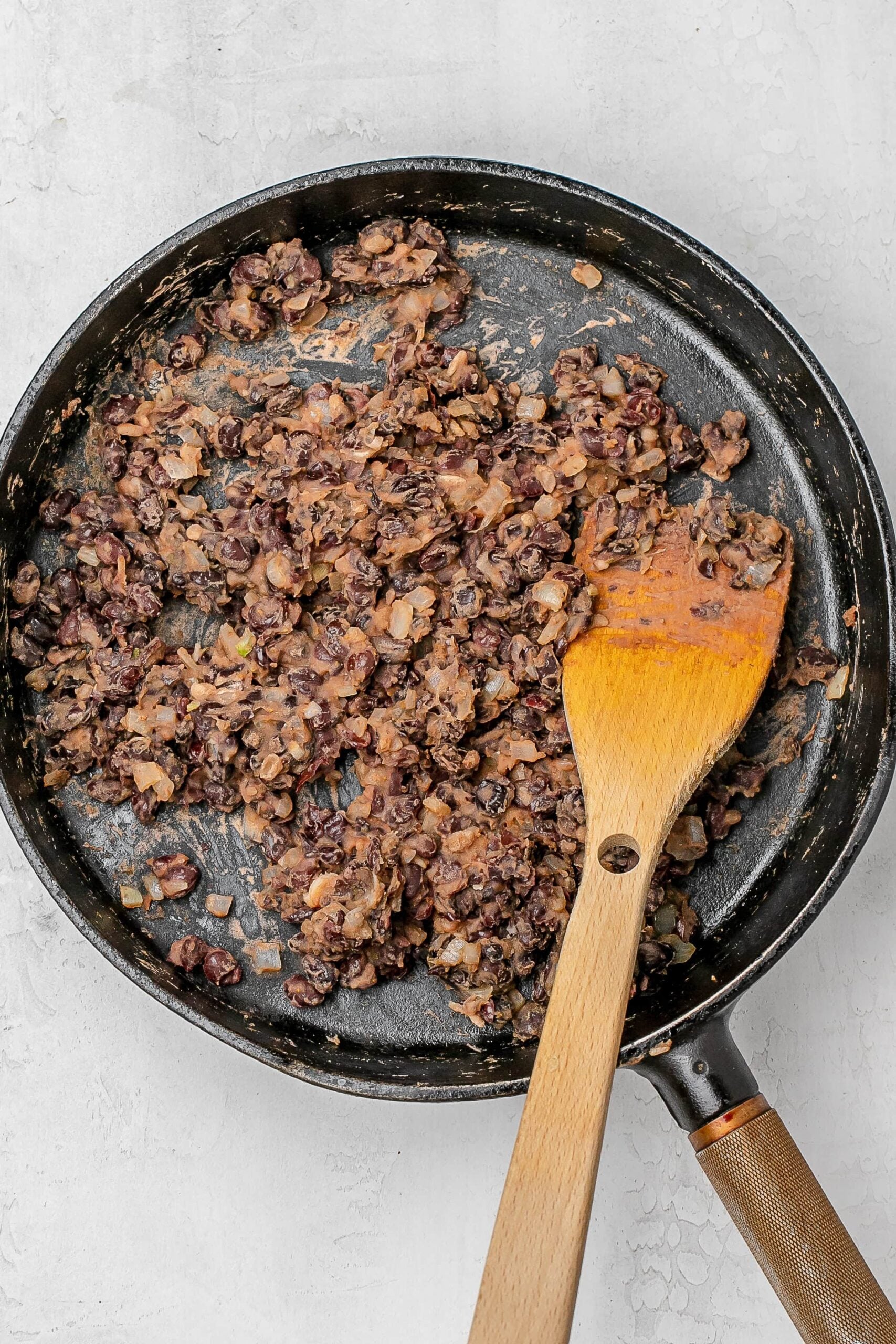 mashed black beans in a cast iron skillet with a wooden spatula. 