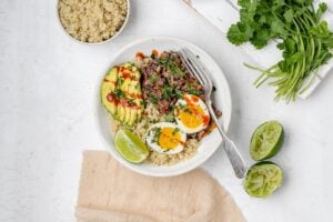 black bean, quinoa and egg breakfast bowl with avocado and hot sauce drizzled on top.