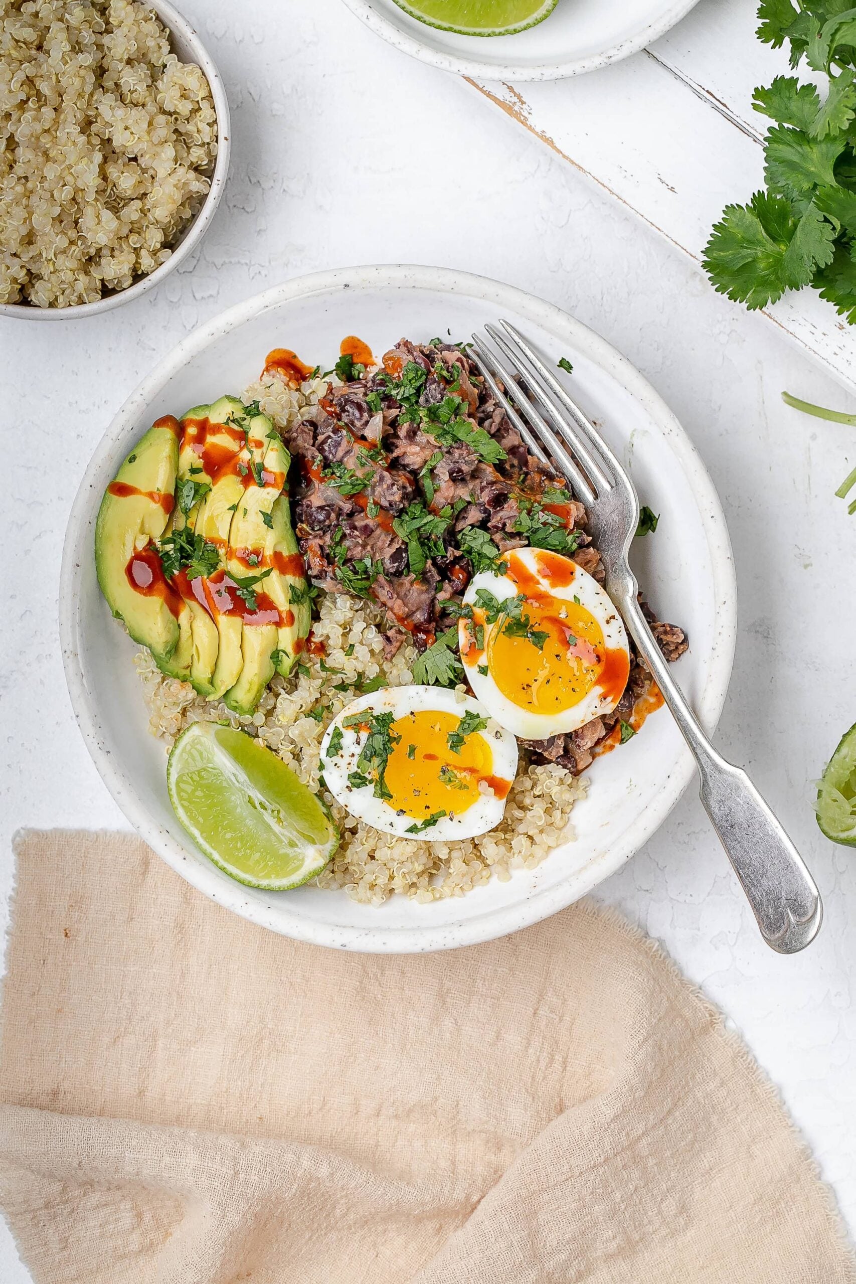 black bean, quinoa and egg breakfast bowl with avocado and hot sauce drizzled on top. 