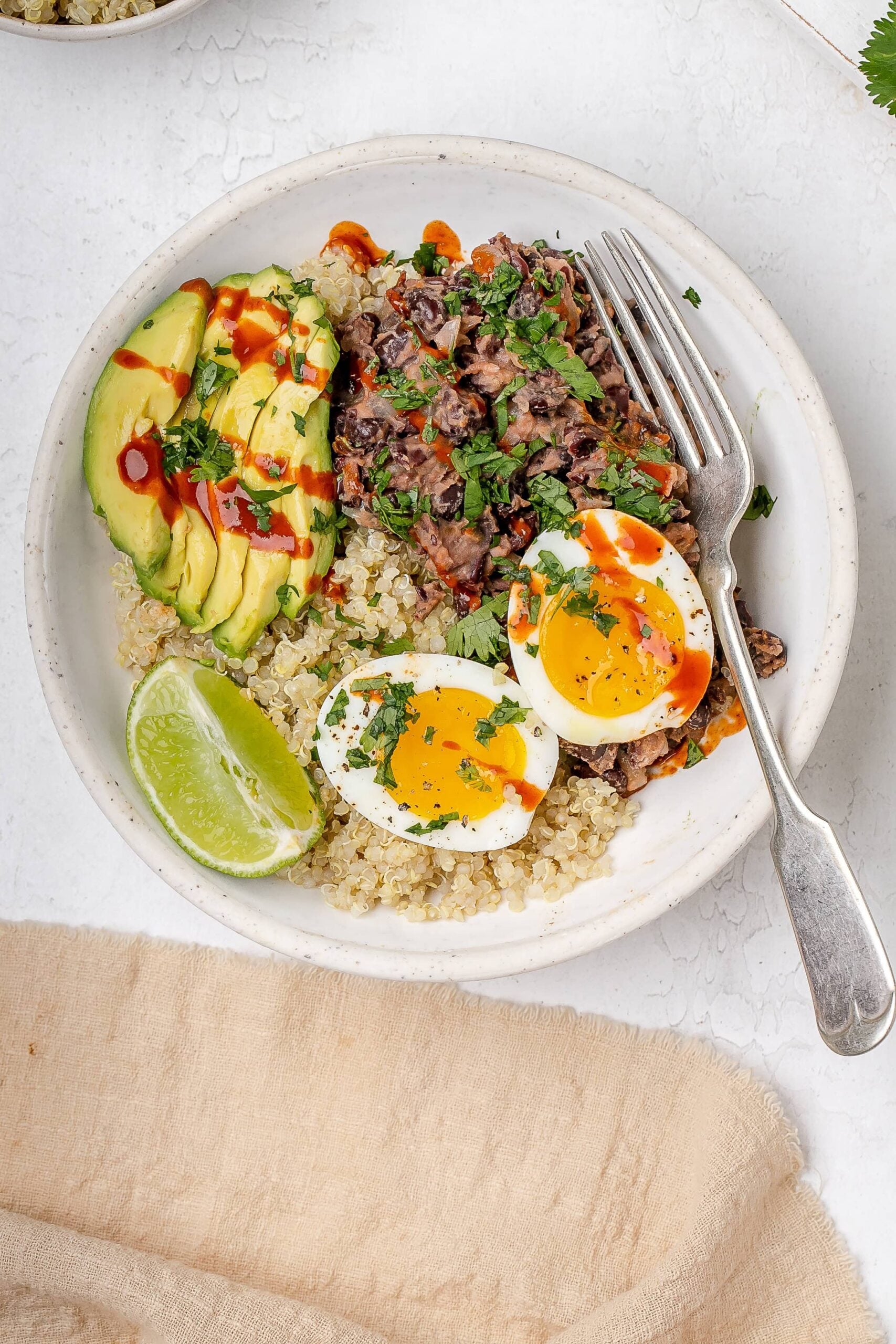 black bean, quinoa and egg breakfast bowl with avocado and hot sauce drizzled on top. 