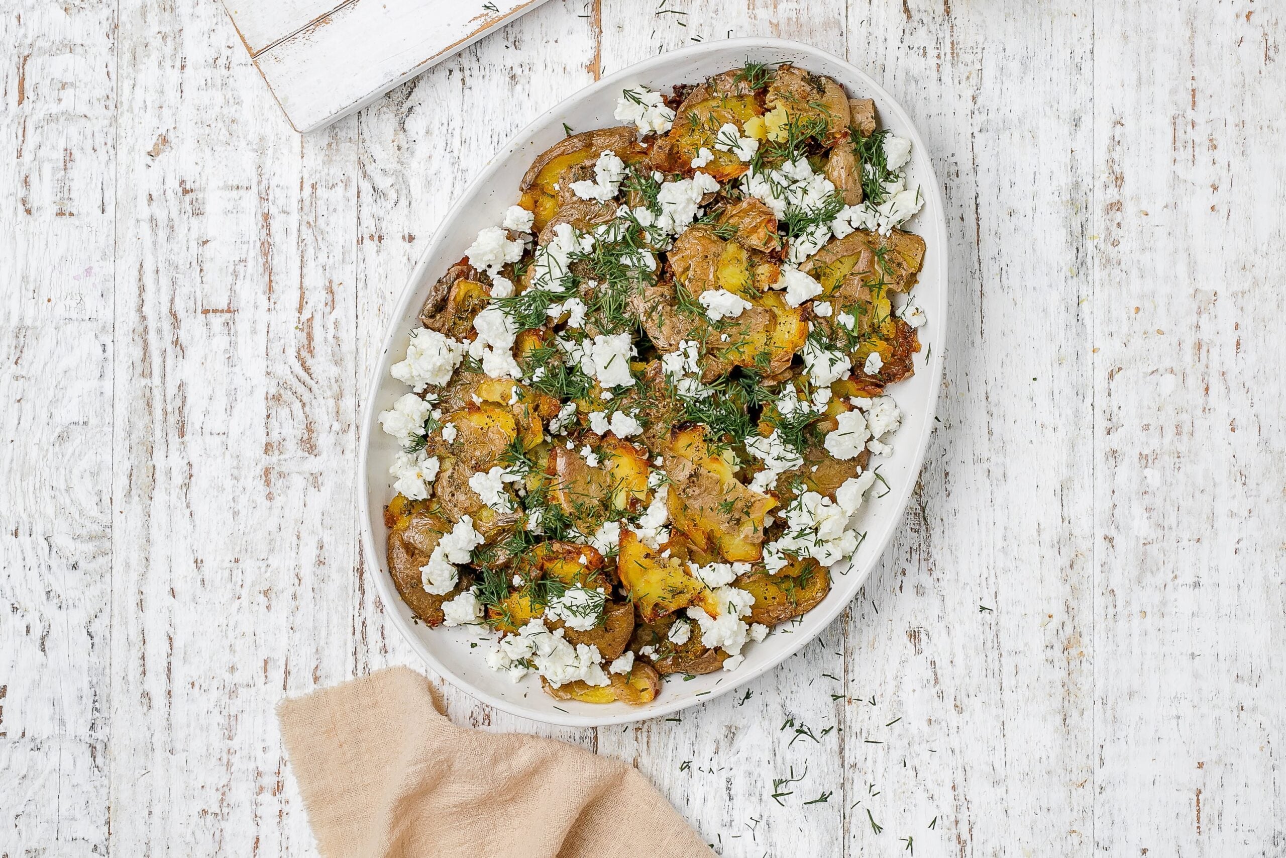 Greek smashed potatoes on a platter with dill and feta.