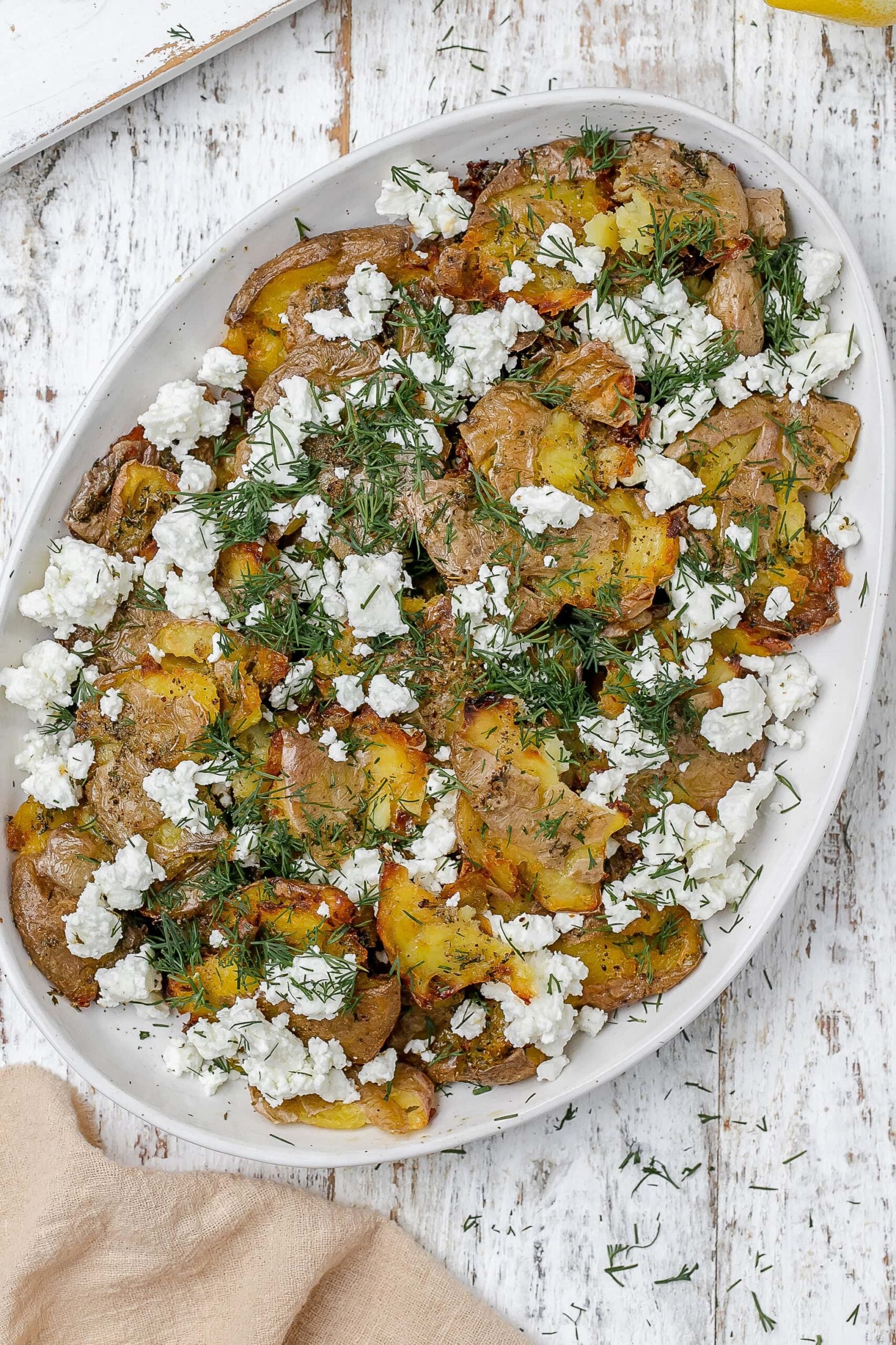 Greek smashed potatoes on a platter with dill and feta.