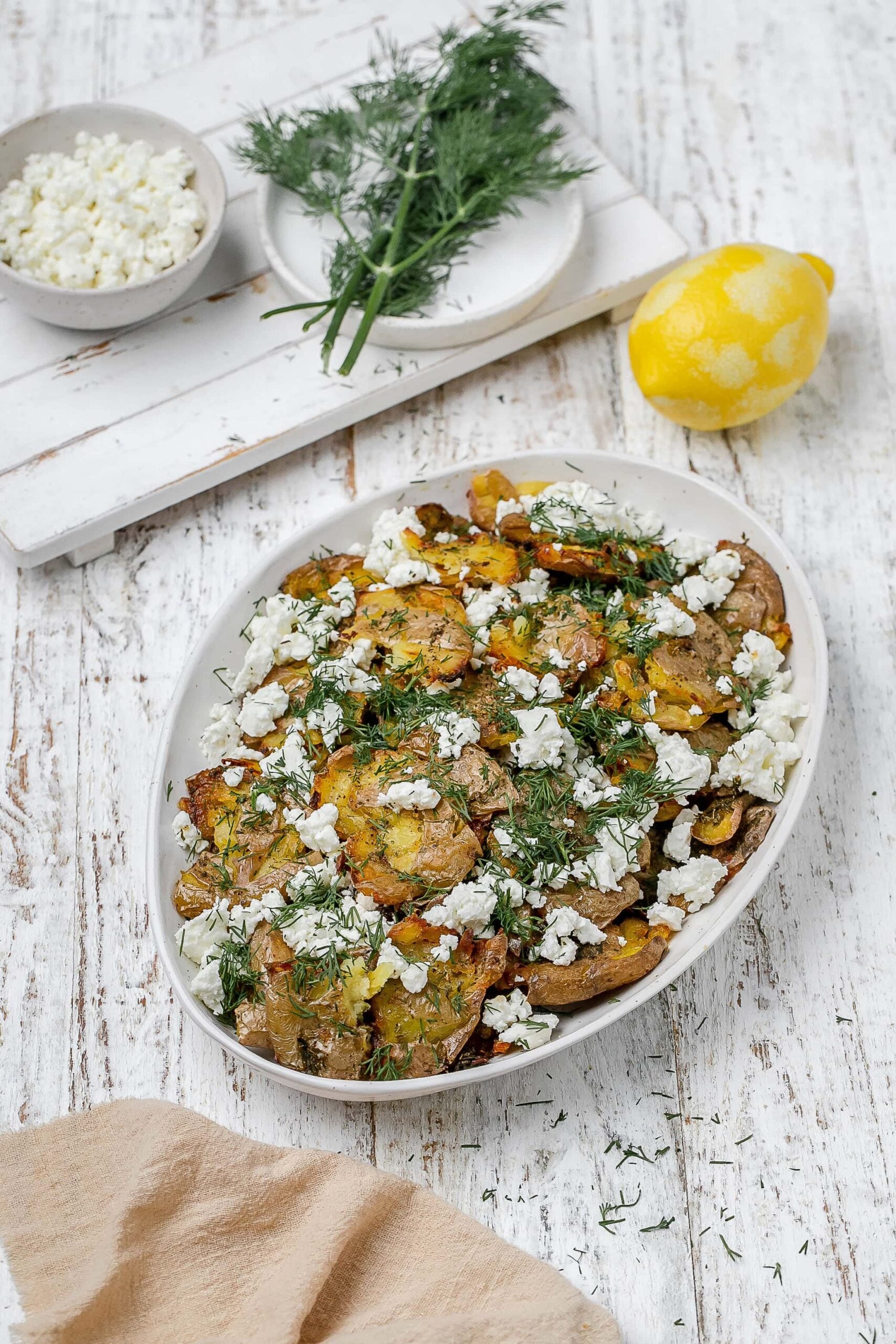 Greek smashed potatoes on a platter with dill and feta.