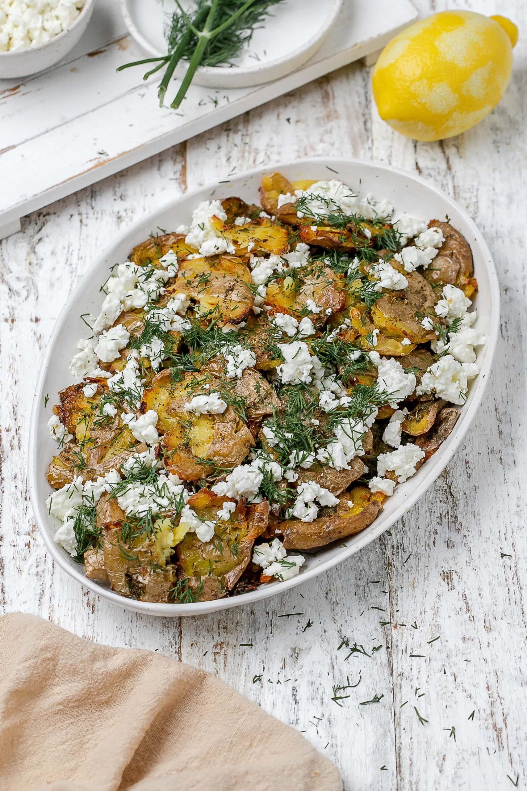 Greek smashed potatoes on a platter with dill and feta.