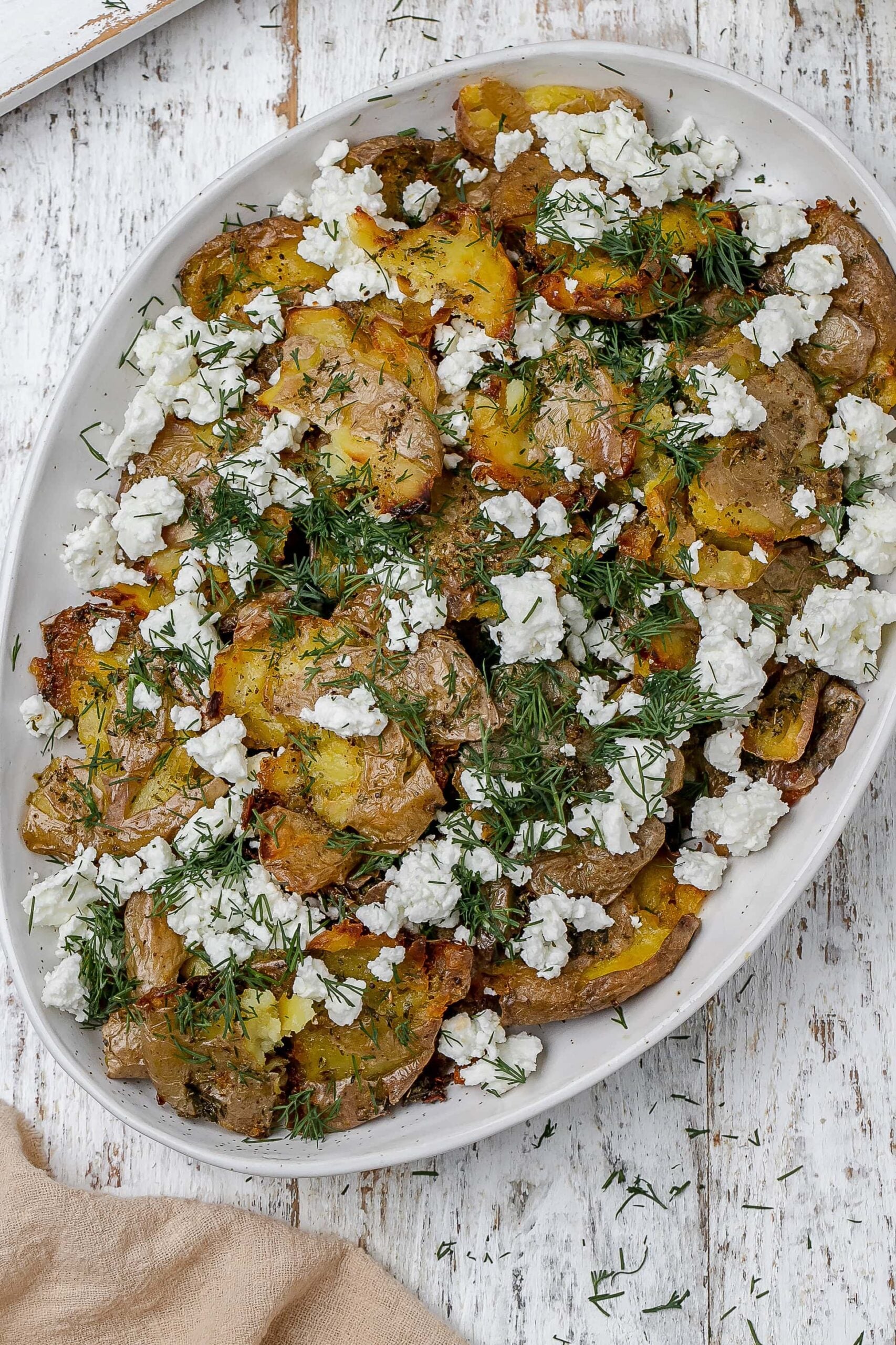 Greek smashed potatoes on a platter with dill and feta.