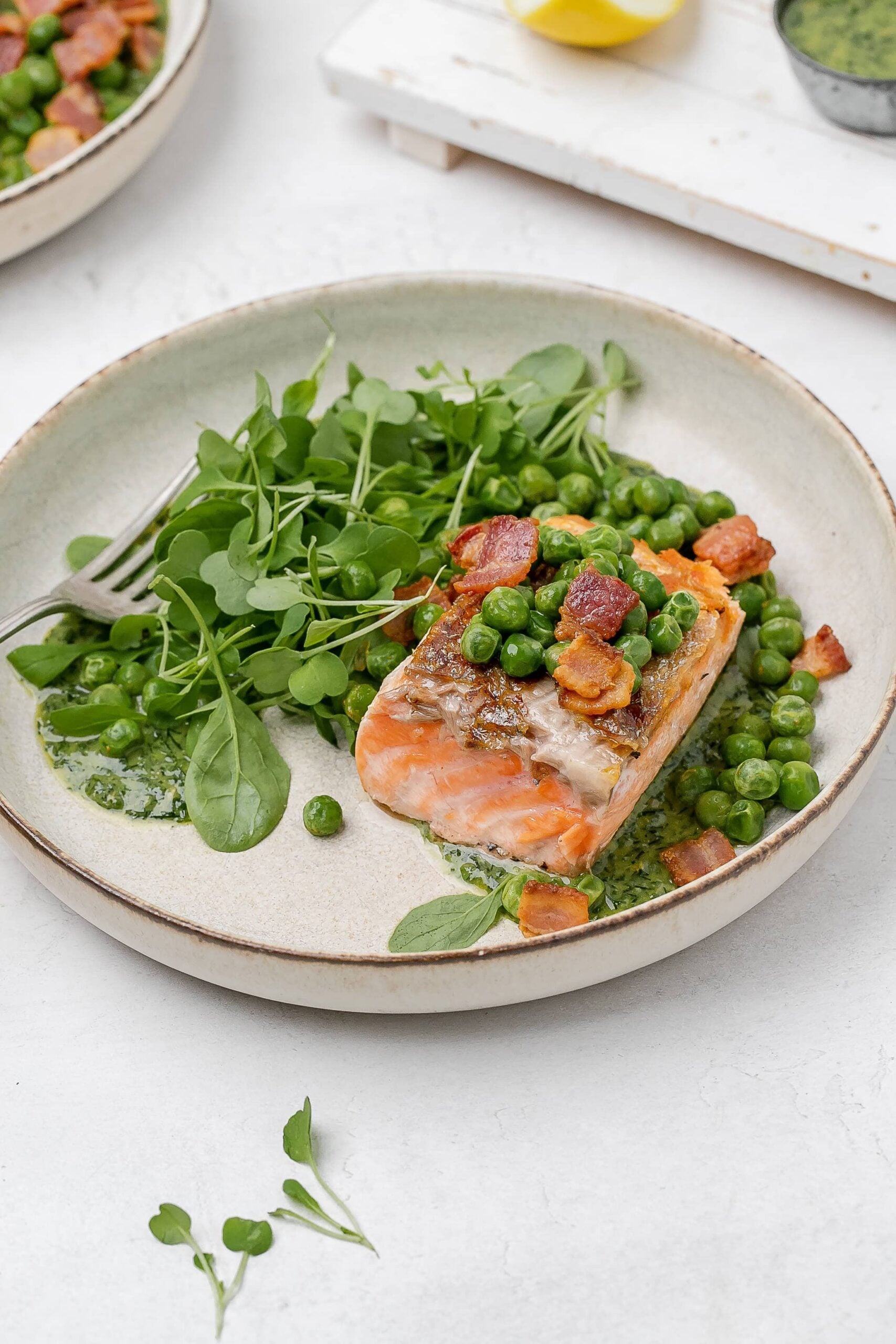 salmon with peas, bacon and greens on a plate. 