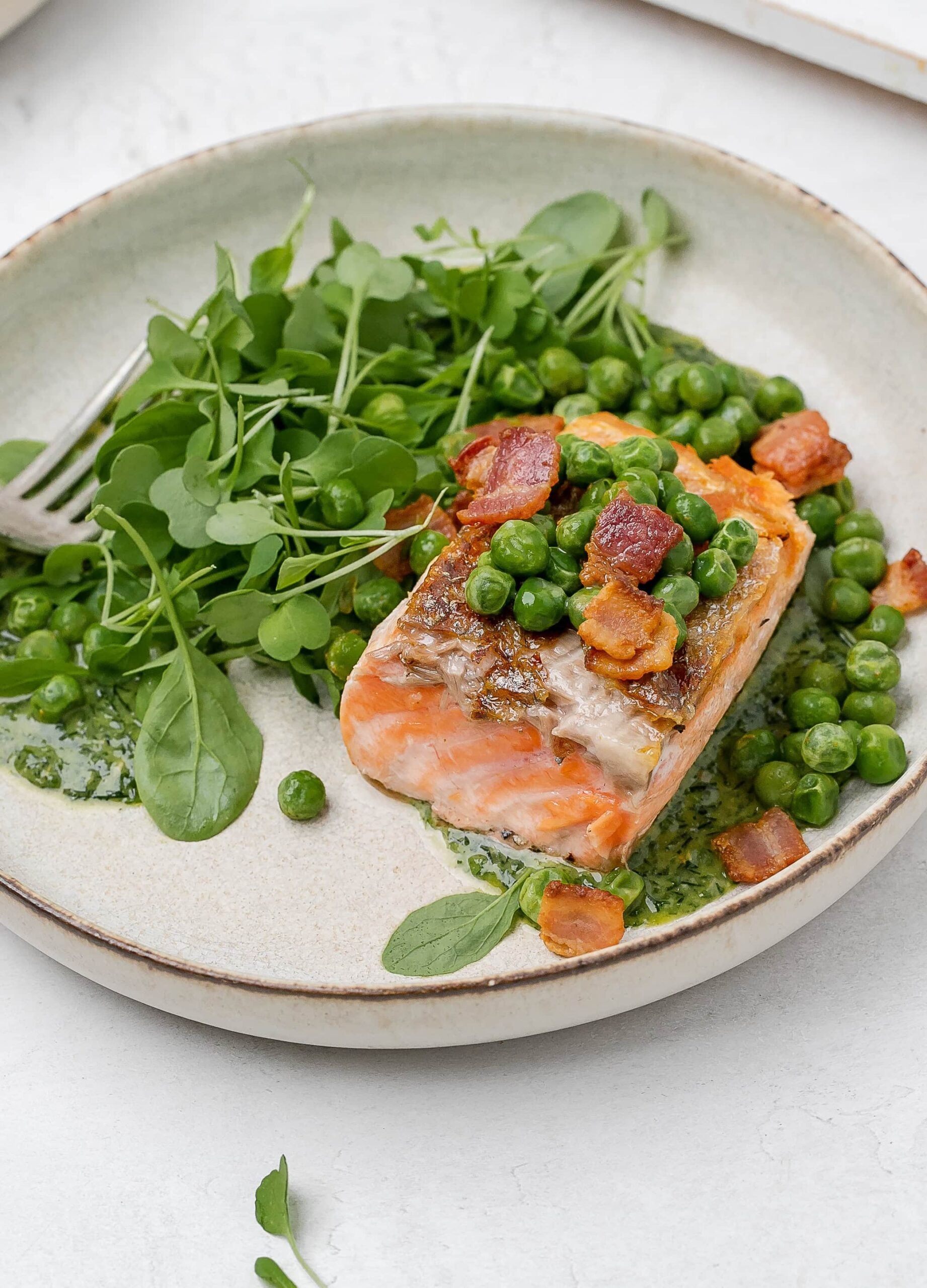 salmon with peas, bacon and greens on a plate. 