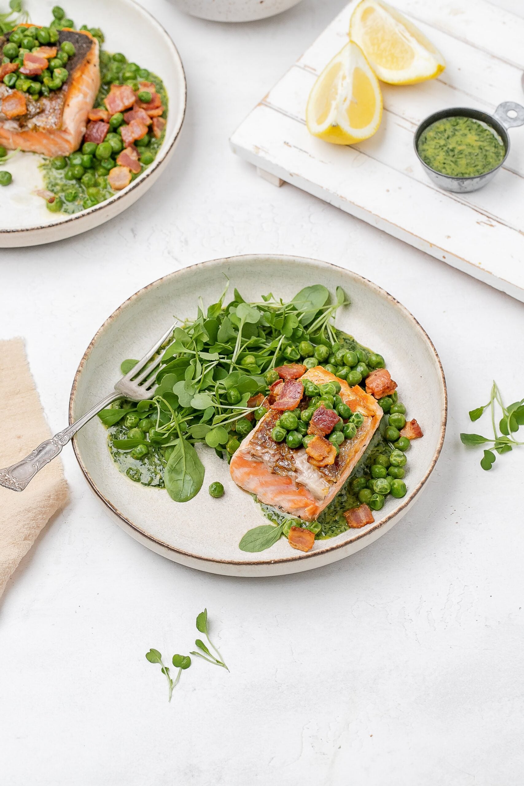 salmon with peas, bacon and greens on a plate. 