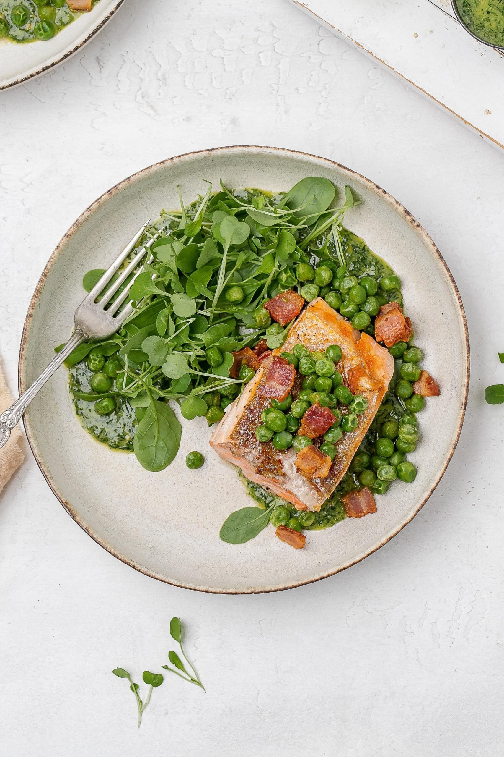 salmon with peas, bacon and greens on a plate. 