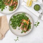 salmon with peas, bacon and greens on a plate.
