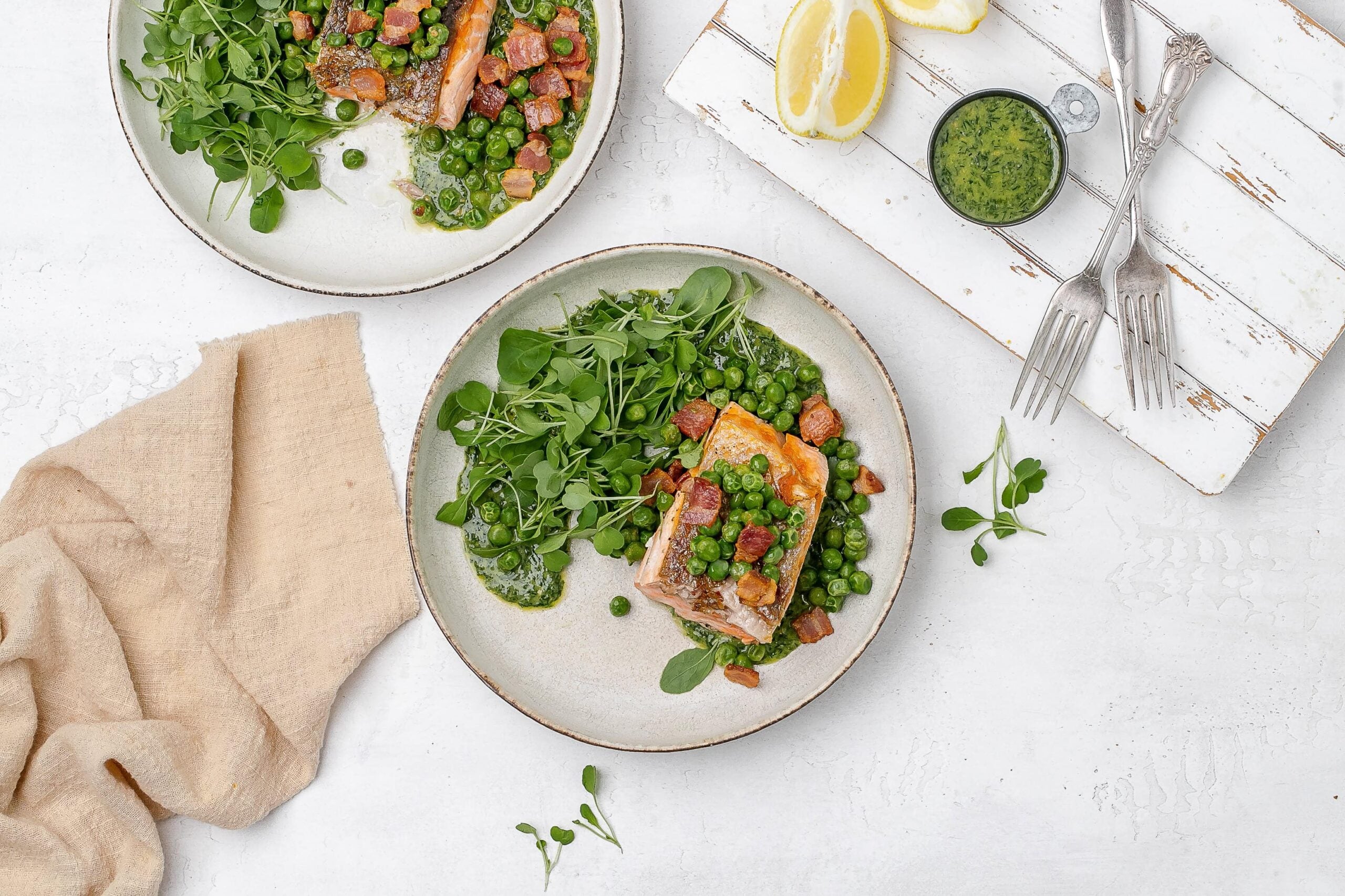 salmon with peas, bacon and greens on a plate.
