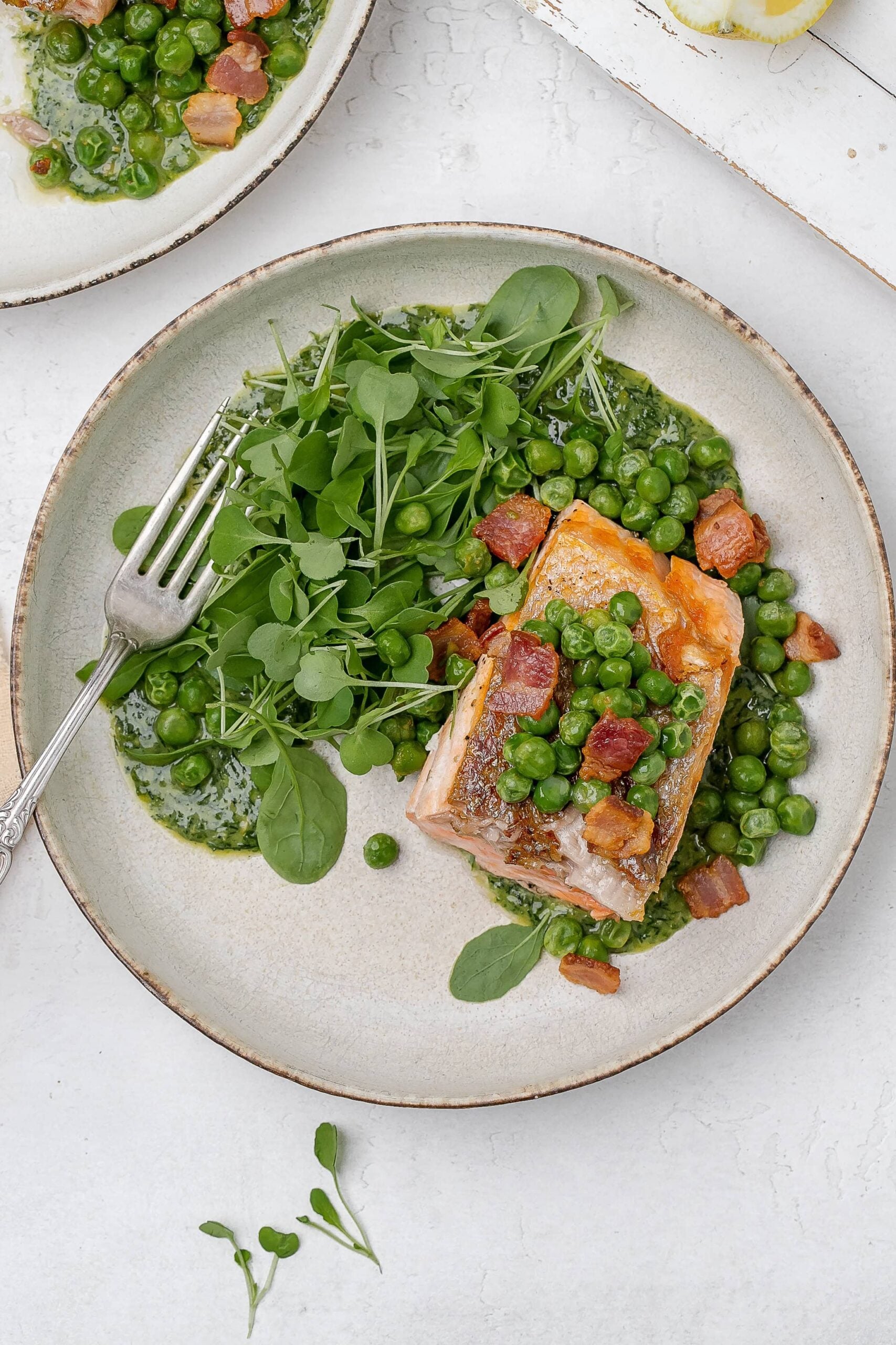 salmon with peas, bacon and greens on a plate. 