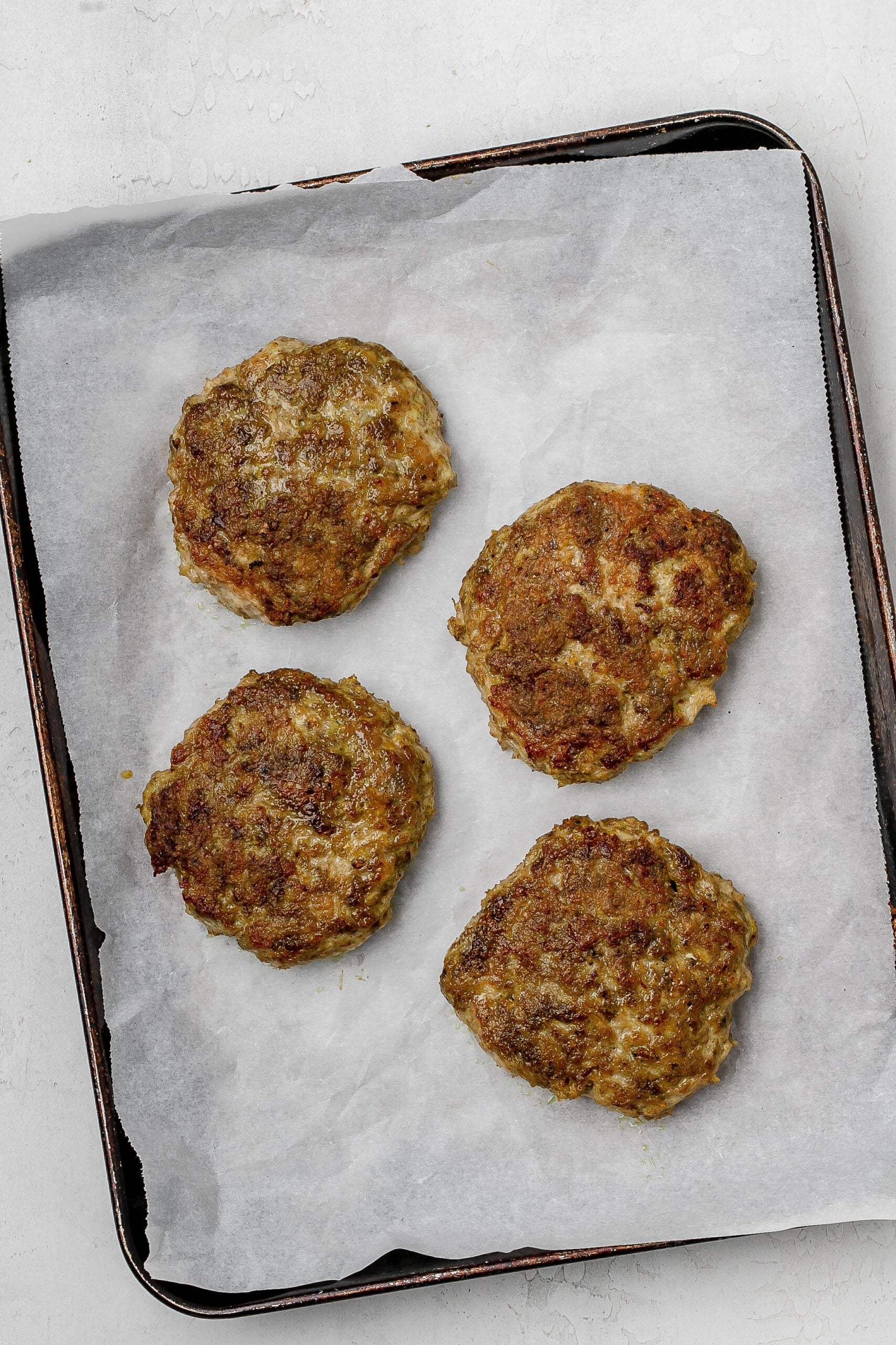 chicken burger patties on a parchment lined baking sheet.