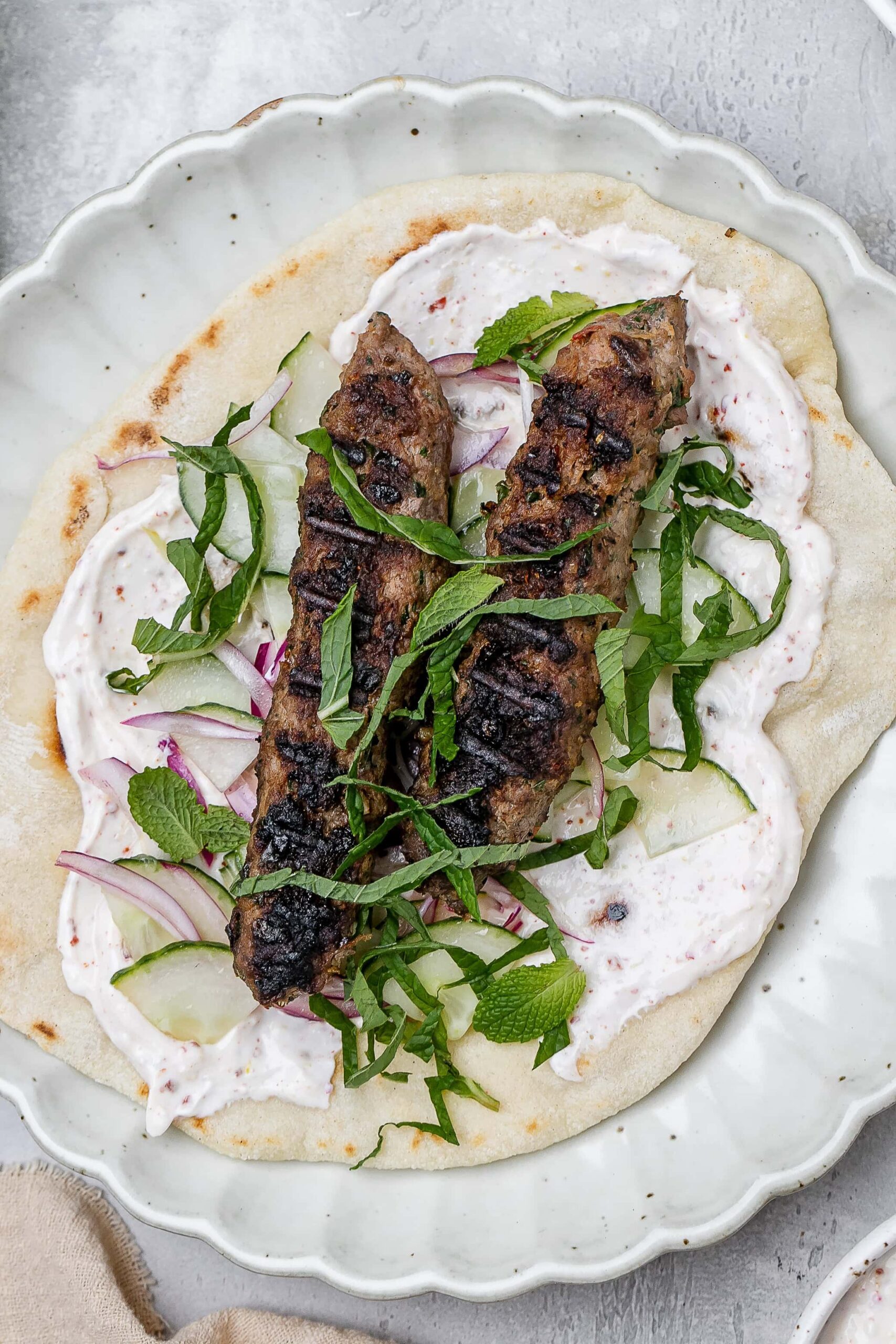 beef and lamb kofta skewers on a pita with toppings.