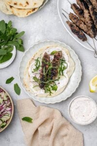 beef and lamb kofta skewers on a pita with toppings.
