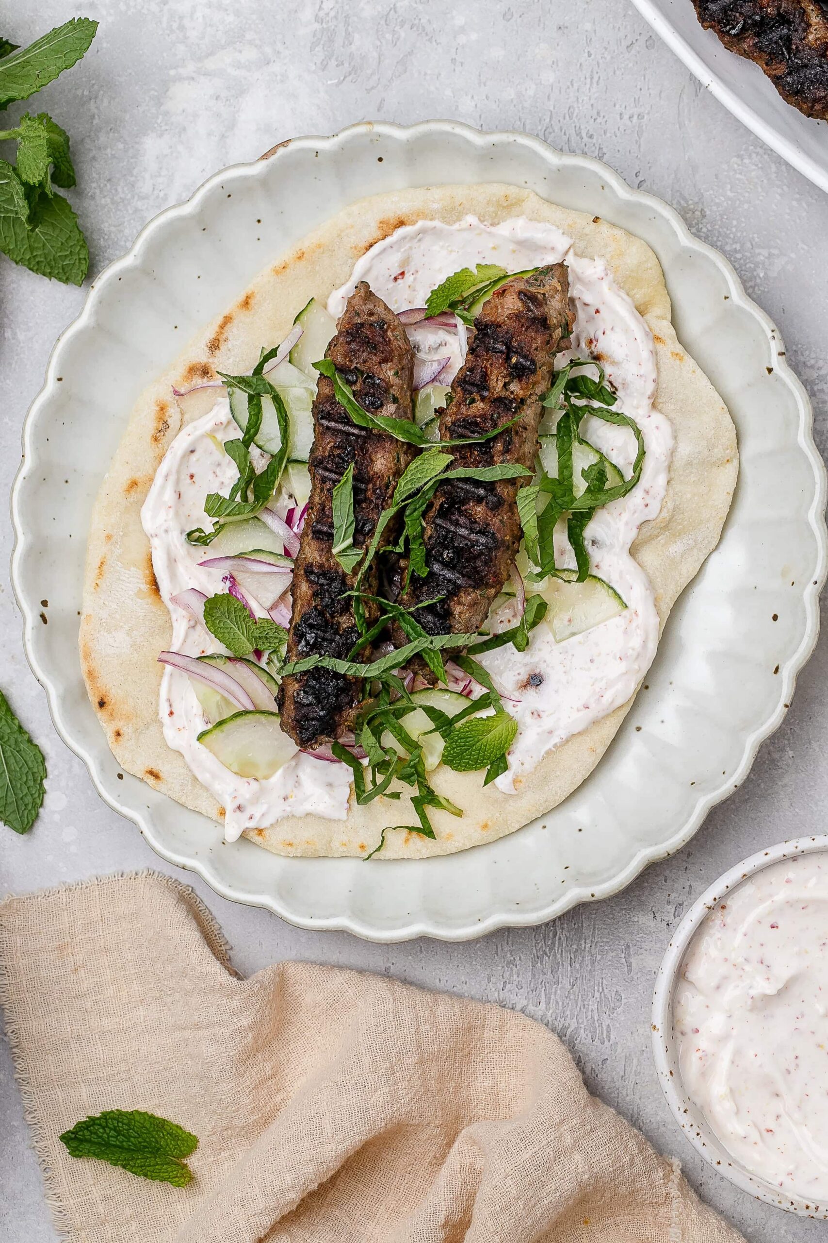 beef and lamb kofta skewers on a pita with toppings.