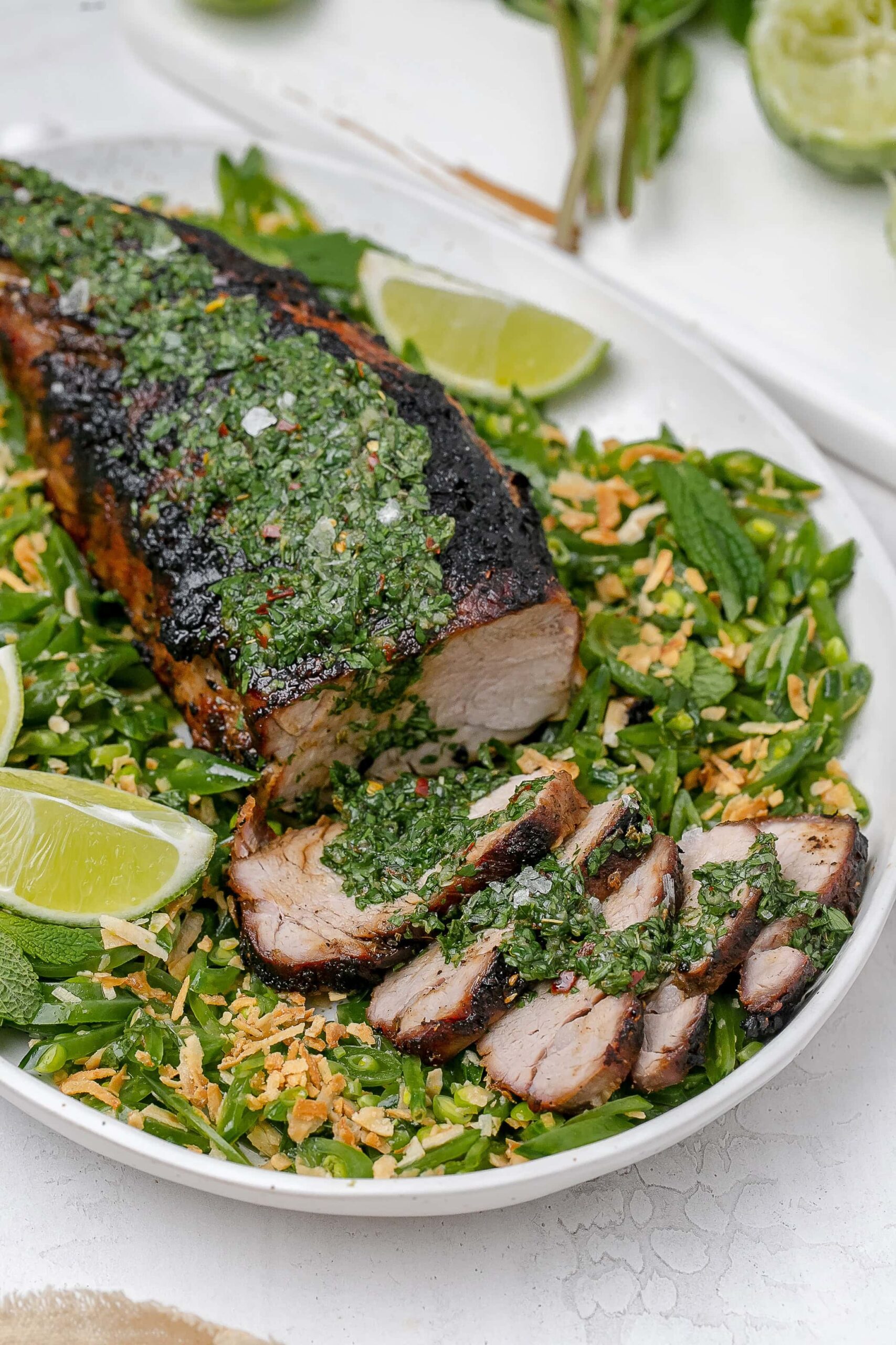 grilled pork tenderloin with chimichurri on top and peas surrounding it.
