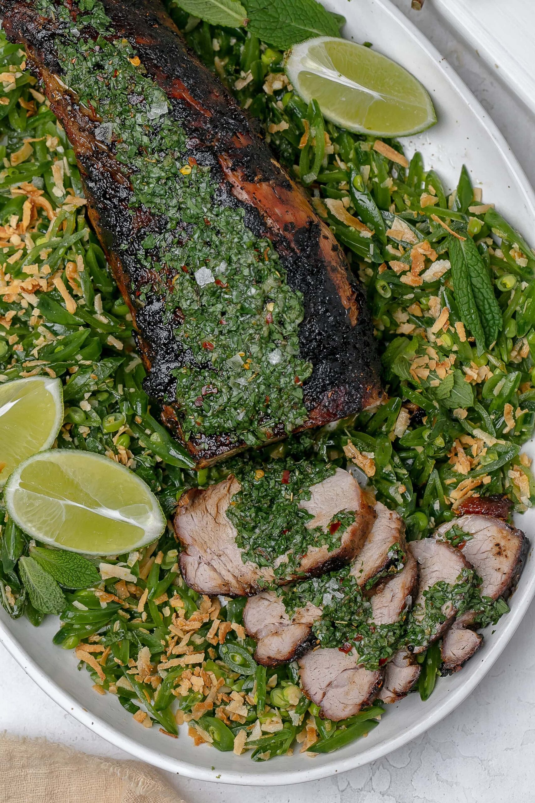 grilled pork tenderloin with chimichurri on top and peas surrounding it.