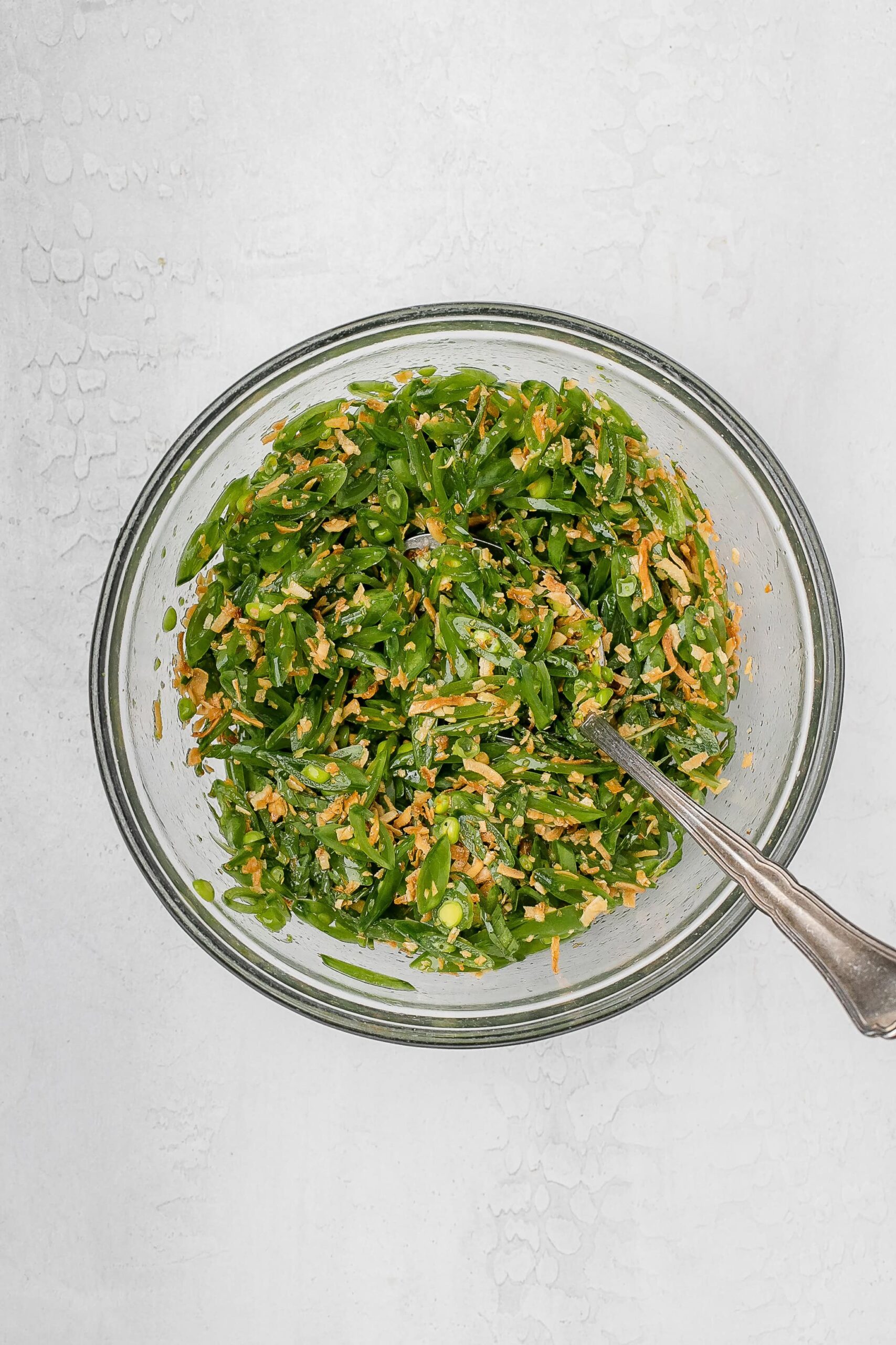 snap peas sliced thinly on a bias in a bowl with dressing and coconut on top.
