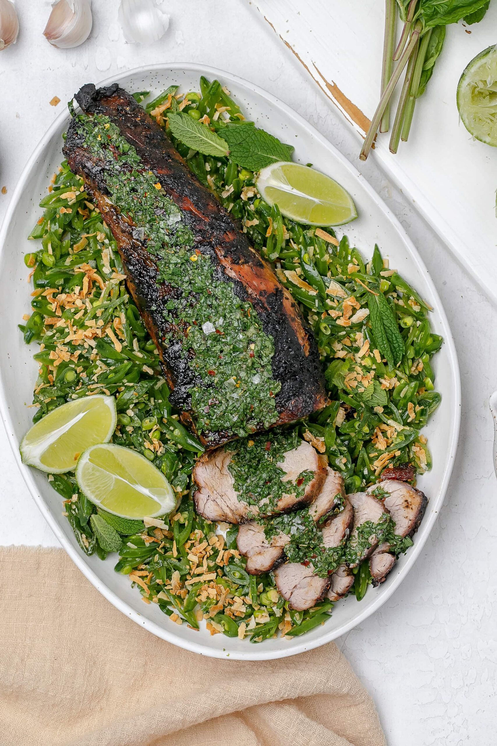 grilled pork tenderloin with chimichurri on top and peas surrounding it.
