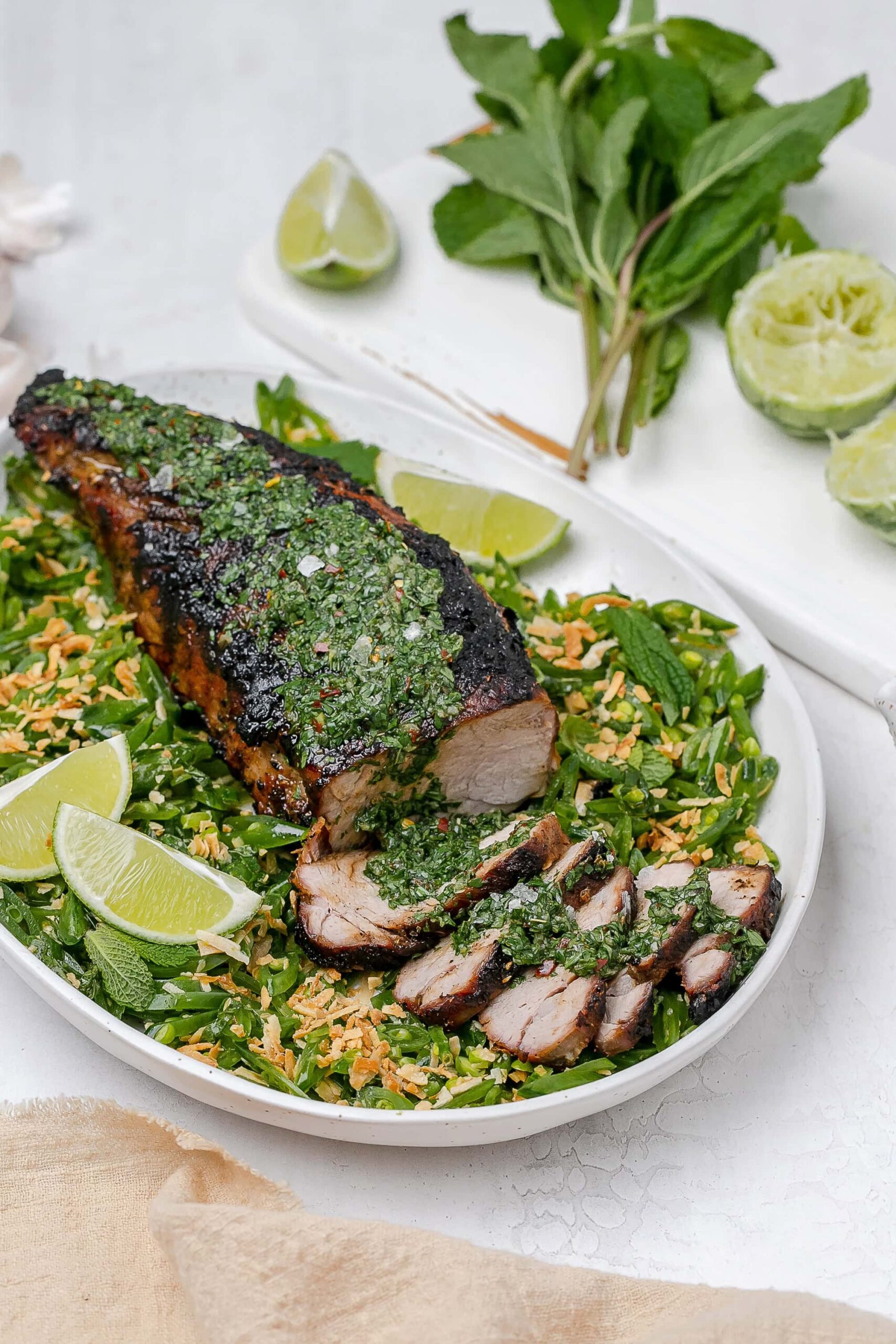 grilled pork tenderloin with chimichurri on top and peas surrounding it.