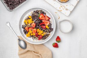 black rice porridge in a bowl with coconut milk and fruit toppings.