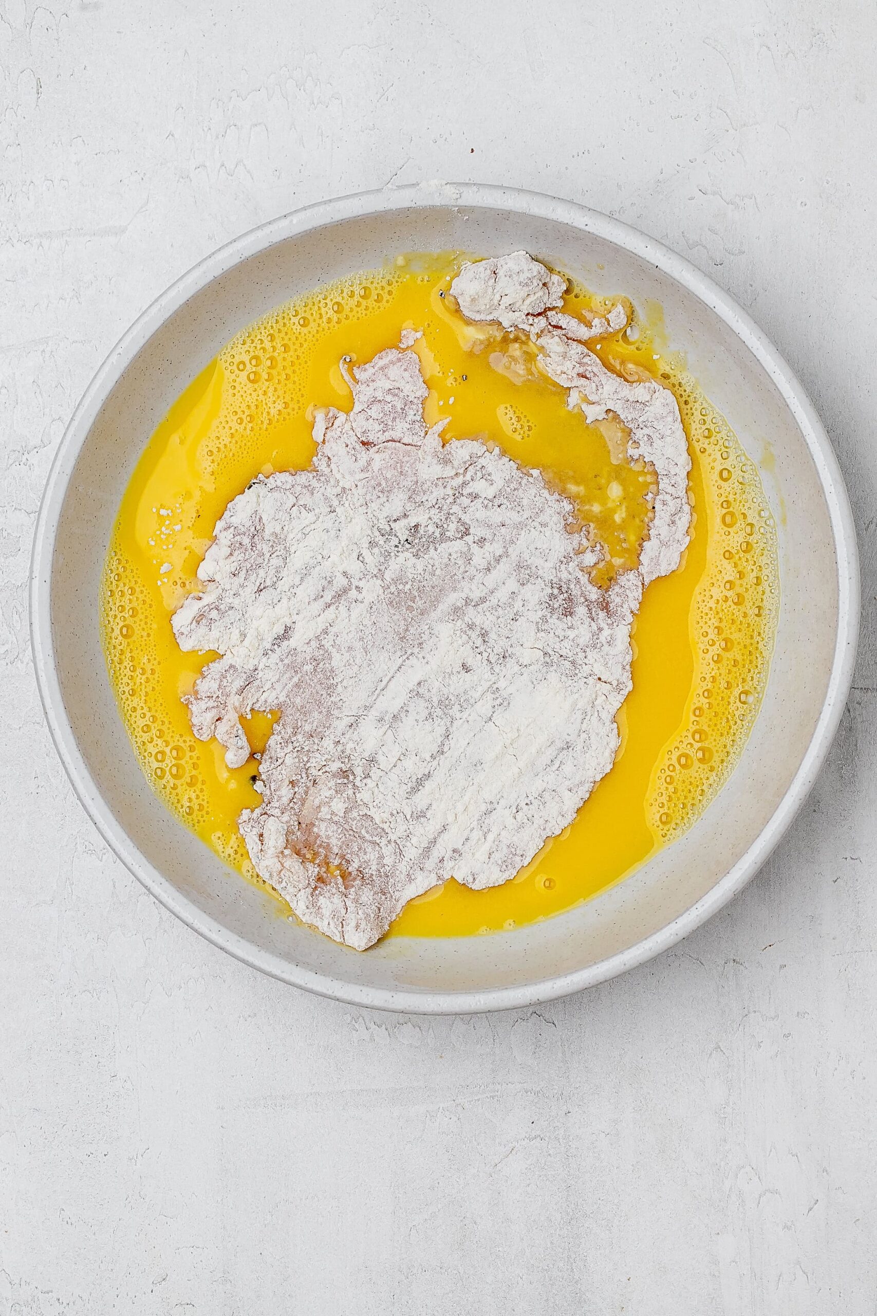 floured chicken in the bowl with the whisked eggs.