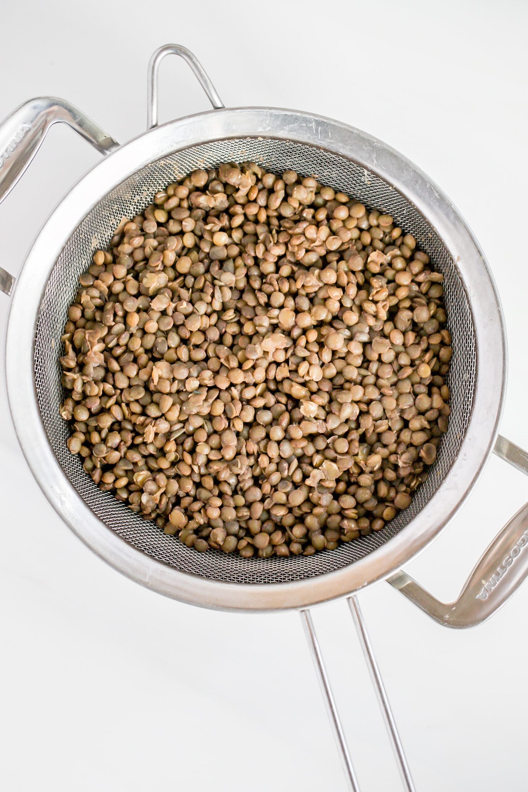 cooked french lentils in a sieve over a pot.