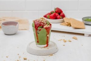 ninja creami matcha ice cream in a glass cup with strawberry sauce and graham crackers on top.