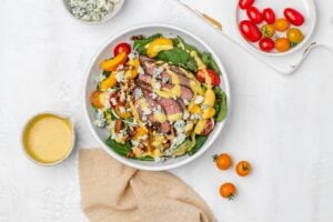 summer steak salad with peaches, blue cheese and dressing in a bowl.