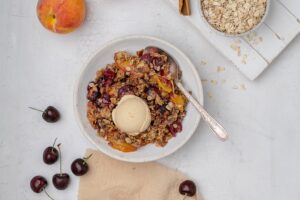 peach and cherry crisp in a bowl with a scoop of ice cream on top.