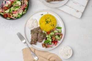 sheet pan beef kofta with rice, salad and yogurt dip on a plate.