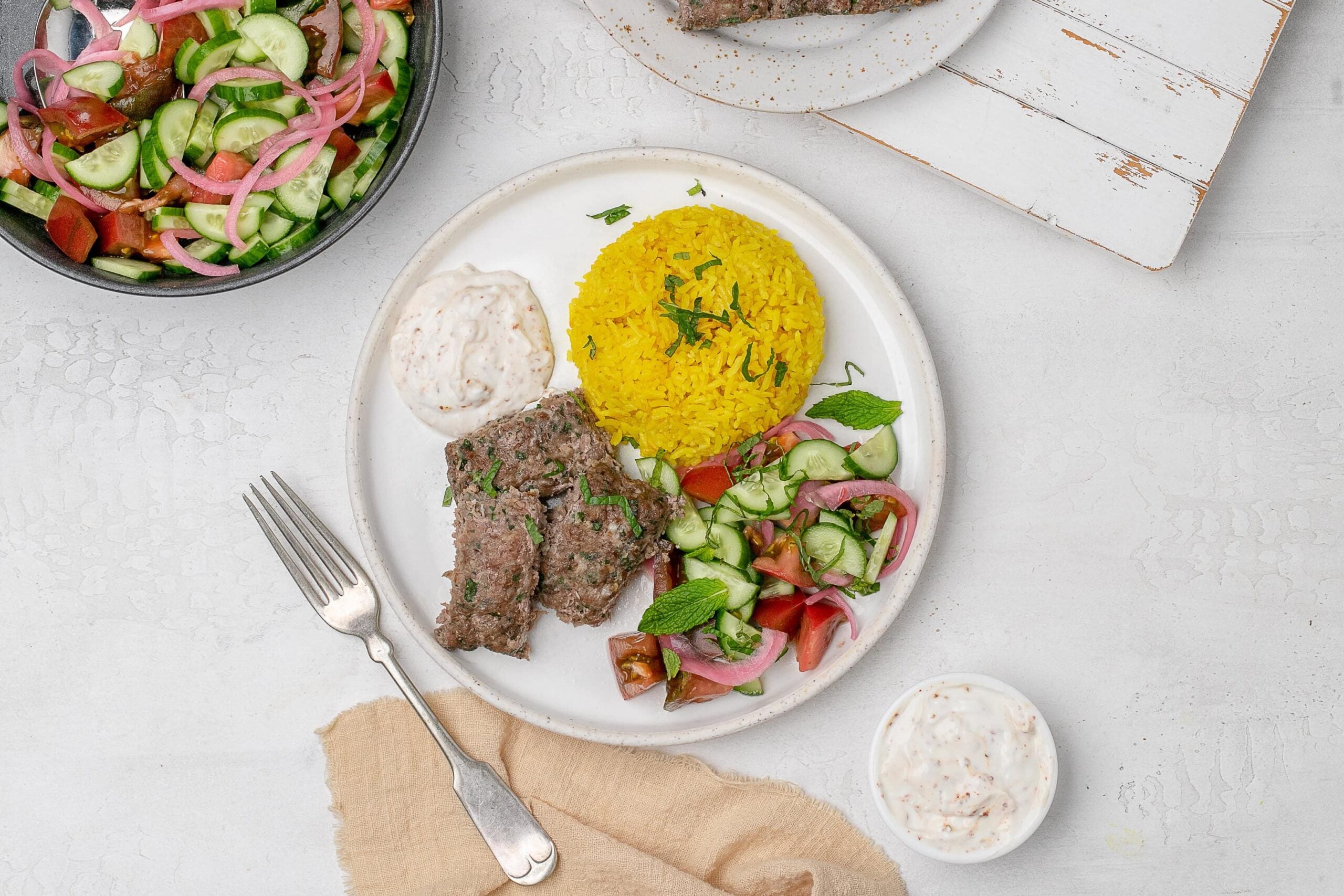 sheet pan beef kofta with rice, salad and yogurt dip on a plate.