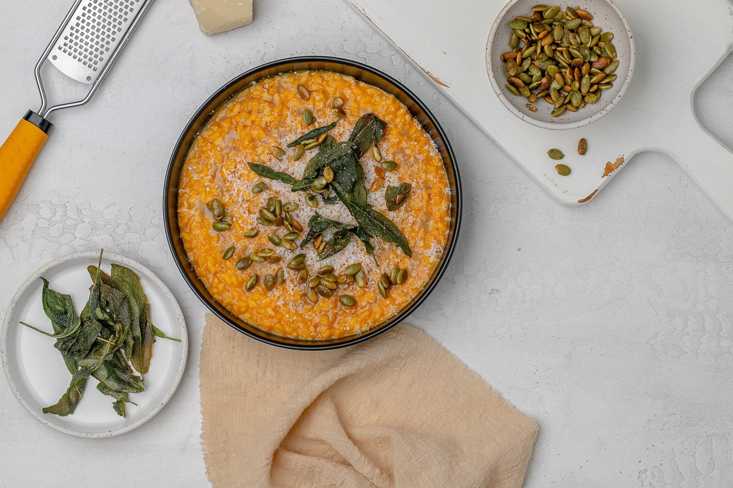 pumpkin risotto in a shallow black bowl with crispy sage, brown butter and pumpkin seeds.