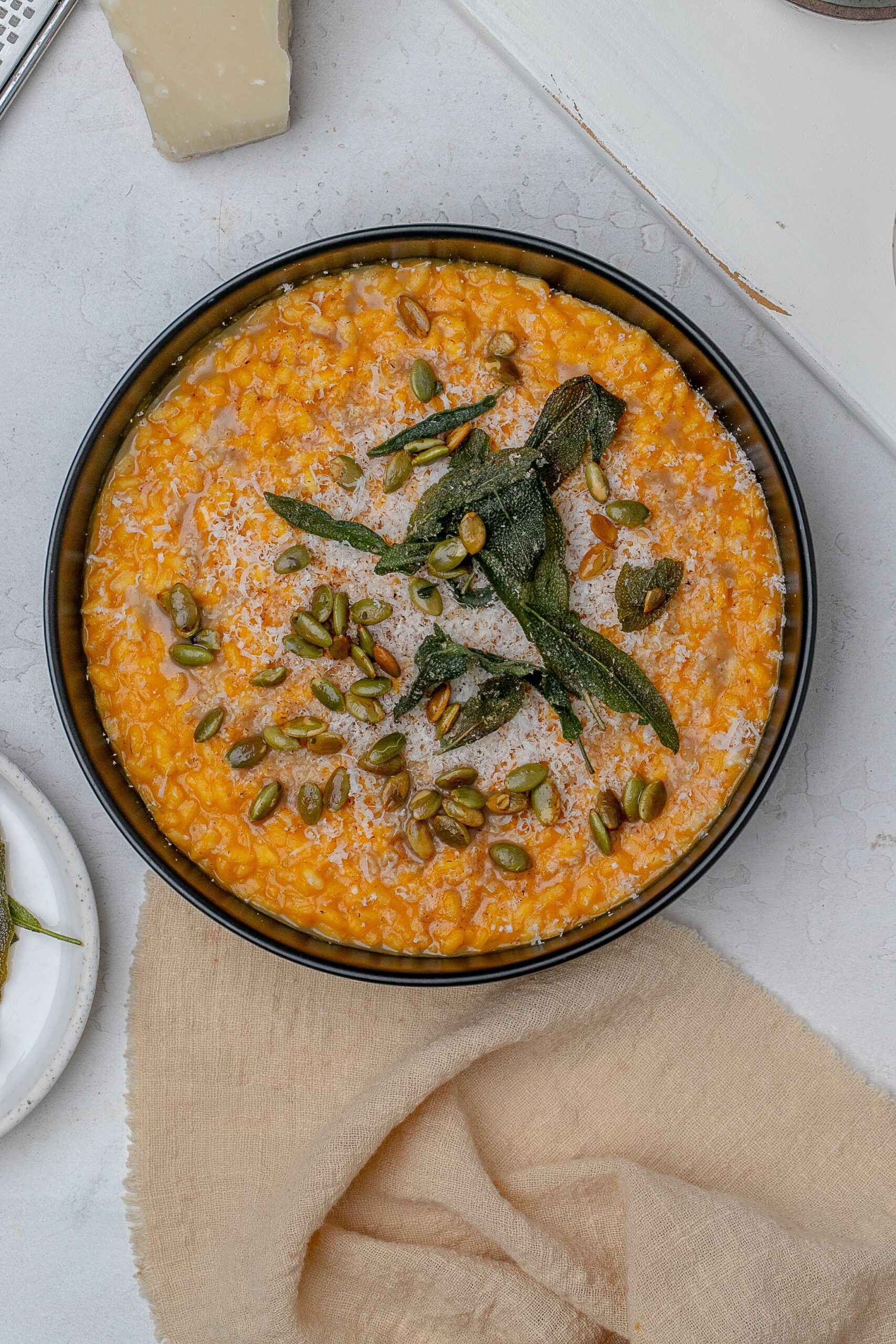 pumpkin risotto in a shallow black bowl with crispy sage, brown butter and pumpkin seeds.
