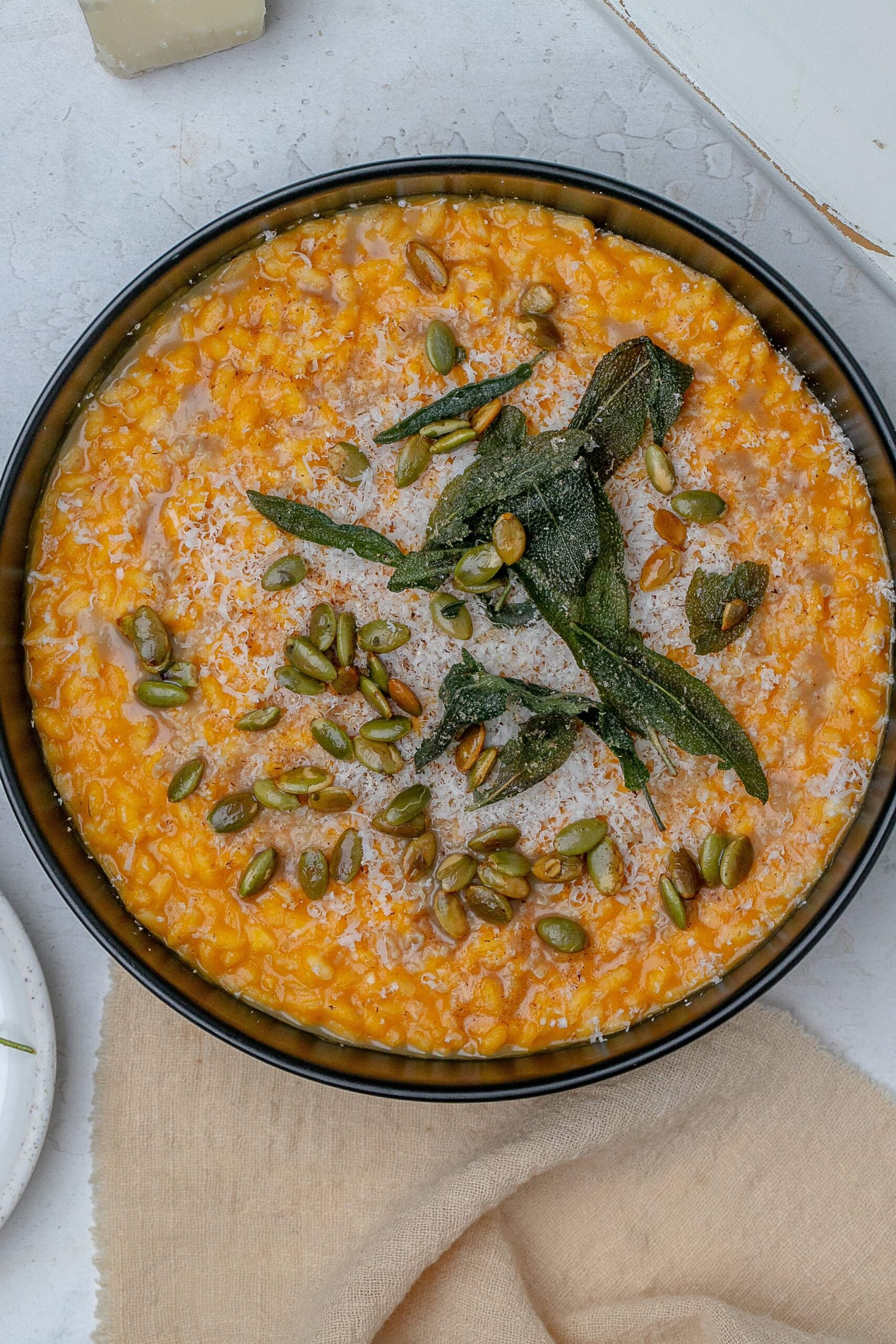 pumpkin risotto in a shallow black bowl with crispy sage, brown butter and pumpkin seeds.