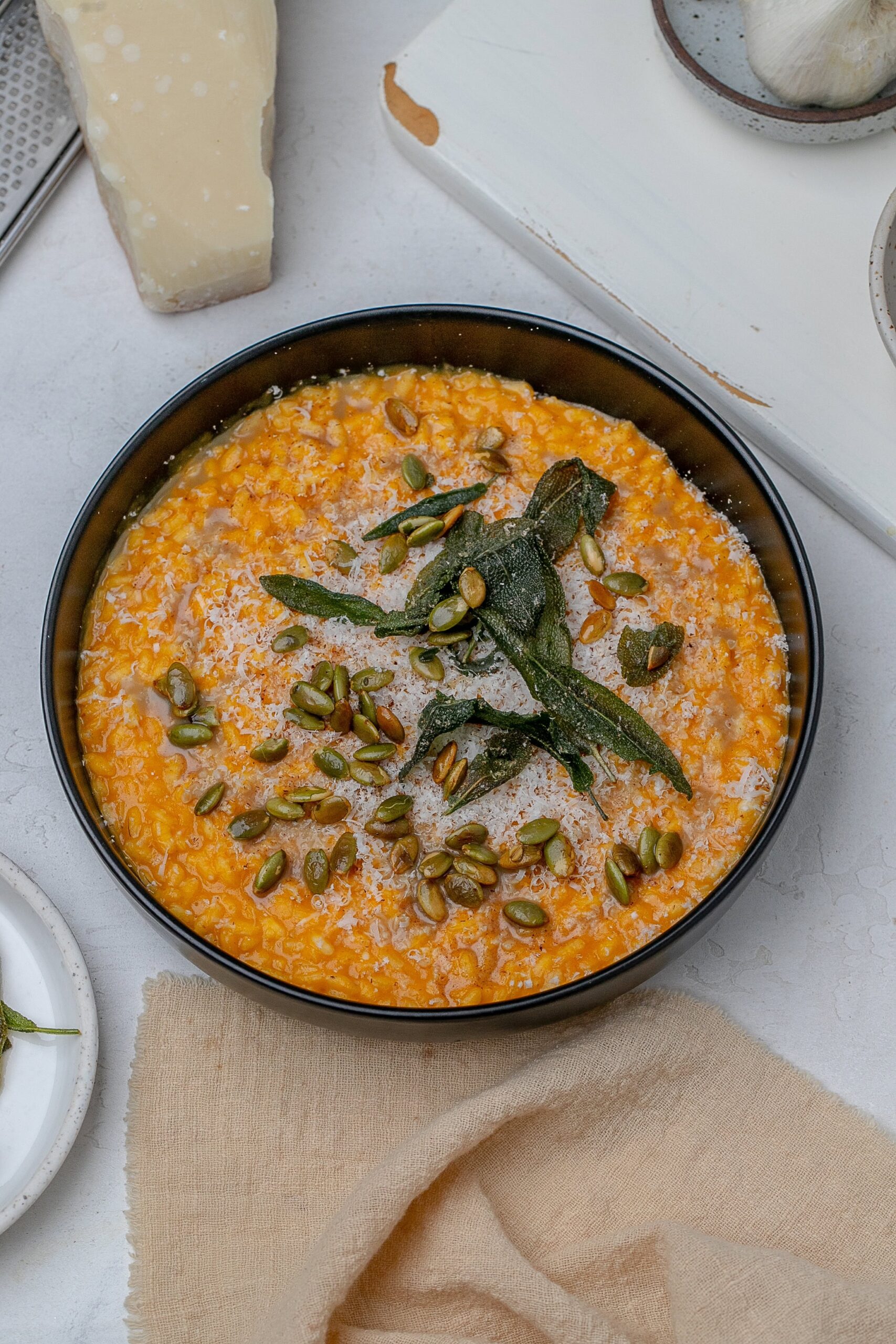pumpkin risotto in a shallow black bowl with crispy sage, brown butter and pumpkin seeds.